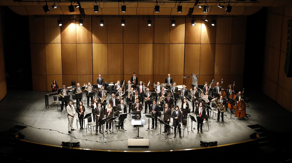 Foto de grupo de músicos saludando al público en un escenario cultural